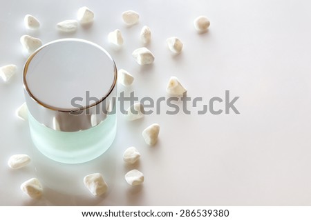 Glass closed jar with facial or body cream on white table with small white stones. Top view. White isolated.