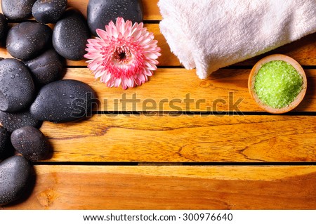Black stones with water drops in the top left corner, flower, towel and bath salts on wooden slats. Sauna and massage concept. Horizontal composition. Top view