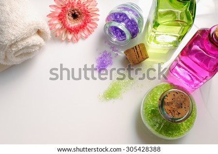 Oils and bath salts on white glass table. Decorated with flower and towel. Horizontal composition. Top view