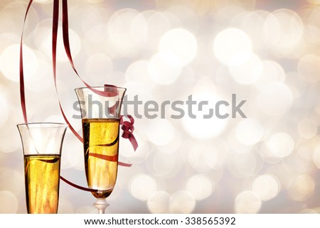 Two glasses of sparkling white wine with bokeh background and red ribbons hanging. Party concept.\
Horizontal composition. Front view