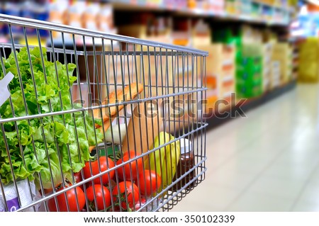 Shopping cart full of food in the supermarket aisle. Side tilt view. Horizontal composition