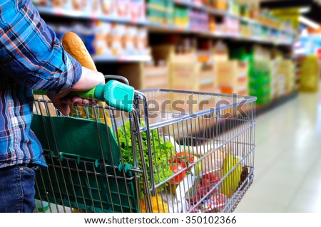 Man pushing shopping cart full of food in the supermarket aisle. Elevated rear view. horizontal composition