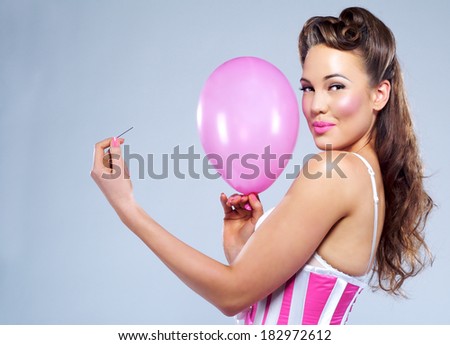 Portrait of a young sensuous woman holding balloon and pin against colored background
