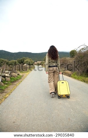 woman with suitcase on rural road at gredos mountains in avila spain