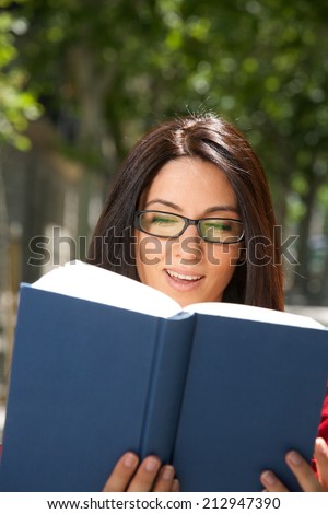 smiling woman with glasses reading a blue big book at street
