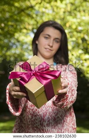 young woman offering golden red gift box over green tree background