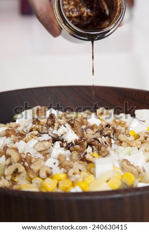 woman hand homemade dressing pot on mixed salad with cheese corn nuts in wooden bowl