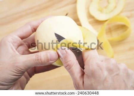 woman hands peeling fresh yellow apple on brown wood plank
