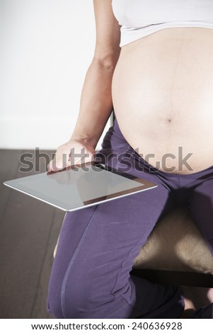 pregnant woman purple trousers bare belly sit showing in her hand blank screen tablet