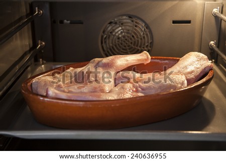 spanish raw leg of baby lamb in brown ceramic tray ready to roast inside oven