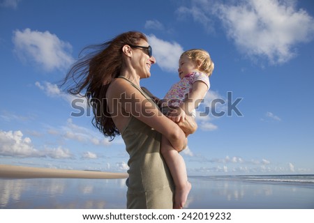 happy green dress woman with sunglasses and one year blonde baby in her arms at beach Conil Cadiz Spain
