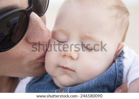 woman black sunglasses kissing three month baby with jeans dress