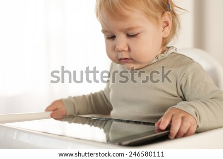 blonde sixteen month baby green sweater using digital tablet inside home