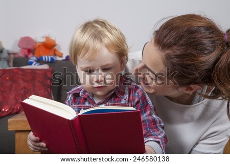 eighteen month aged blonde baby with brunette woman mother reading tale story red book indoor