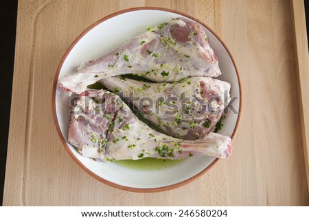 spanish raw legs of baby lamb garlic parsley in white ceramic tray ready to roast