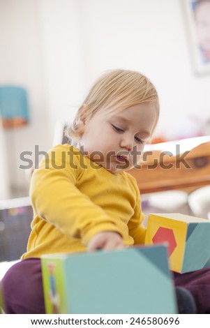 blonde sixteen month baby yellow sweater playing with color boxes inside home