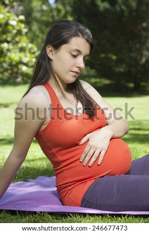 pregnant young woman with orange shirt touching her tummy at a park in Madrid Spain Europe