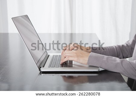 woman hands grey sweater typing in keyboard laptop computer blank screen on black reflect table white curtain indoor