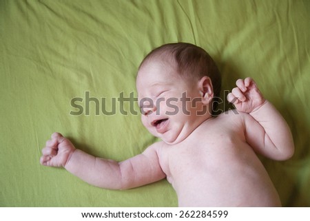 twenty days age baby naked bare crying or smiling close eyes tongue over green sheet bed