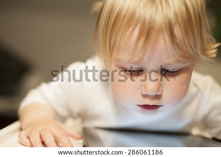 blonde nineteen month age baby white sweater looking at close digital tablet inside home