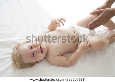 one year blonde baby naked crying over white bedcover with mom arms