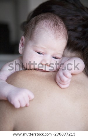portrait of twenty days age baby naked bare embraced open eyes looking with arms on shoulder of brunette woman mother cradling