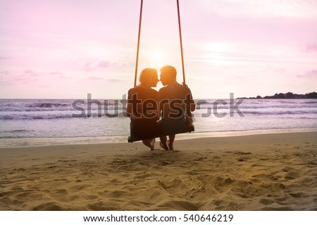 Romantic couple is sitting and kissing on sea beach on rope swing . Family vacation on honeymoon. Love and relationship