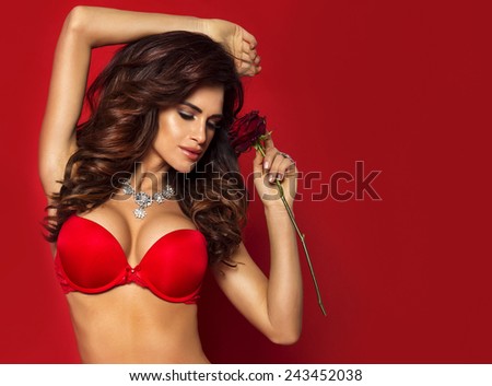 Portrait of beautiful sensual brunette woman with long curly hair. Girl holding red rose.
