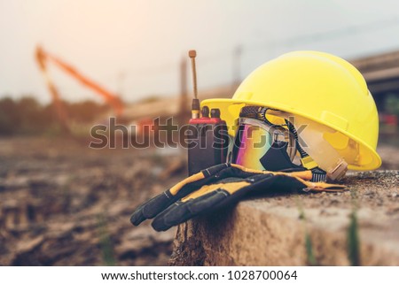 Yellow helmets, gloves, radio communication and safety glasses placed on the cement floor are the background of the construction of blurred buildings.