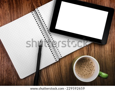 Tablet pc with an empty screen in hands close to a pen and green cup