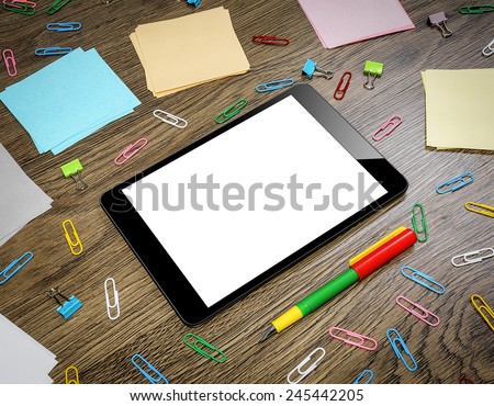 Tablet PC on the office table surrounded by multi-colored paper clips and notebooks