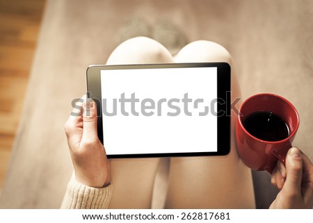 Woman on the sofa with tablet and cup of coffee in hands. Toned photo.