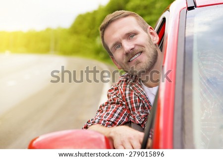 Driver. Happy smiling man in new red car on the road.