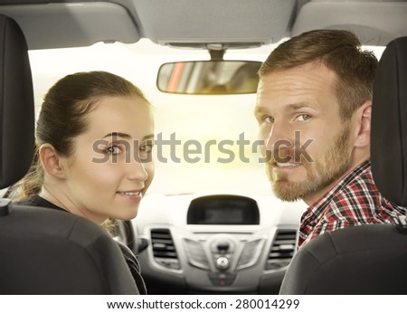 Handsome couple looking at camera sitting in a car, view from rear seat.