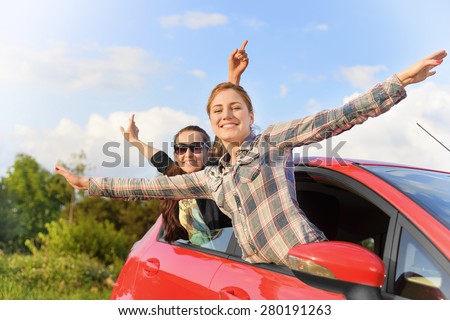 Happy beautiful young girls in a red car in the sunset. Travel concept.