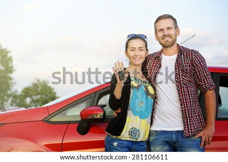 Portrait of happy attractive beautiful couple showingh the keys standing near the red car