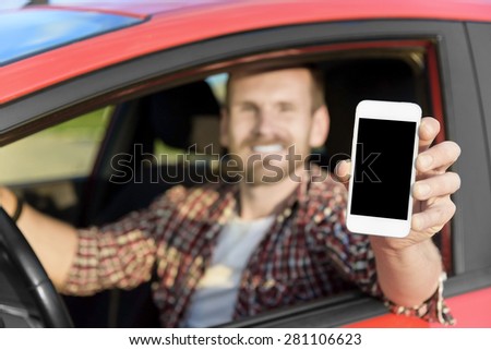 Man in car driving showing smart phone display smiling happy. Focus on smartphone.