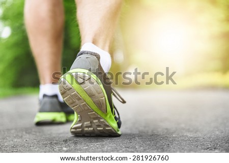 Athlete runner feet running on road closeup on shoe. Man fitness sunrise jog workout wellness concept.