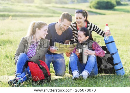 Group hikers on the grass with backpack watching the map, summer outdoor.