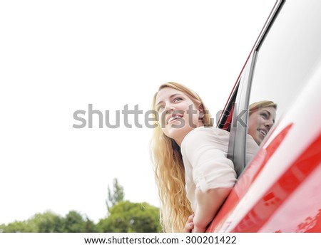 Smiling pretty blonde woman in red car. She looks out the car window.