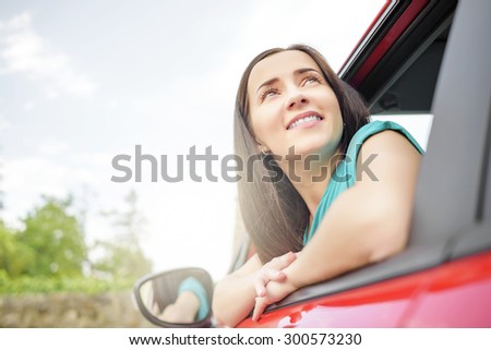 Smiling pretty woman in red car and looks out the car window.