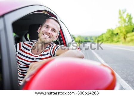 Driver. Smiling man in red car on the road at sunset.
