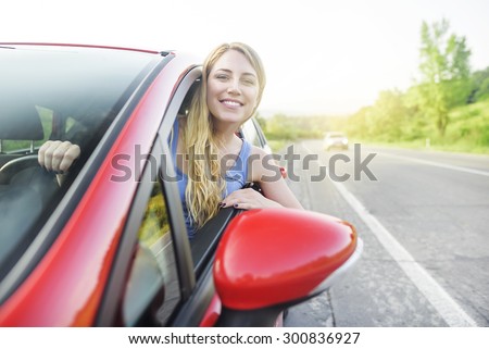 Travel concept. Attractive smiling girl in a red car. At sunset.