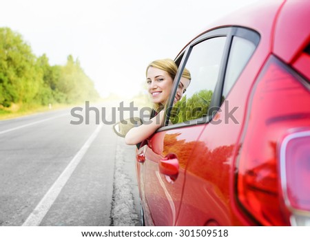 Travel concept. Happy smiling girl in a red car at sunset.