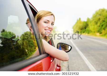 Travel concept. Happy smiling blonde woman in a red car at sunset.