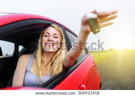 Attractive woman in a car showing keys at sunset.
