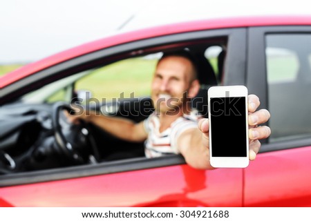 Man in car showing smart phone display smiling happy. Focus on mobile phone.