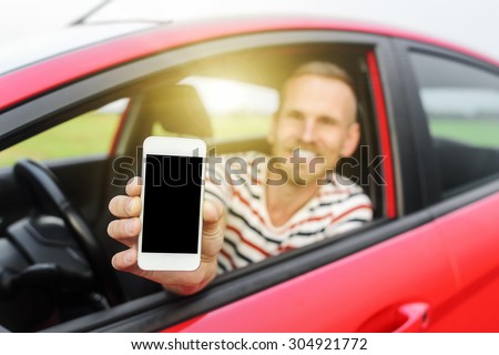 Man in car showing smart phone display smiling happy. Focus on mobile phone.