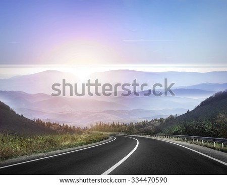 Highway road against mountains and a sky at the sunrise or sunset.