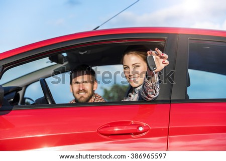 Attractive couple in the red car with the keys of the car at sunset. Concept of travel, rent car or buying car.